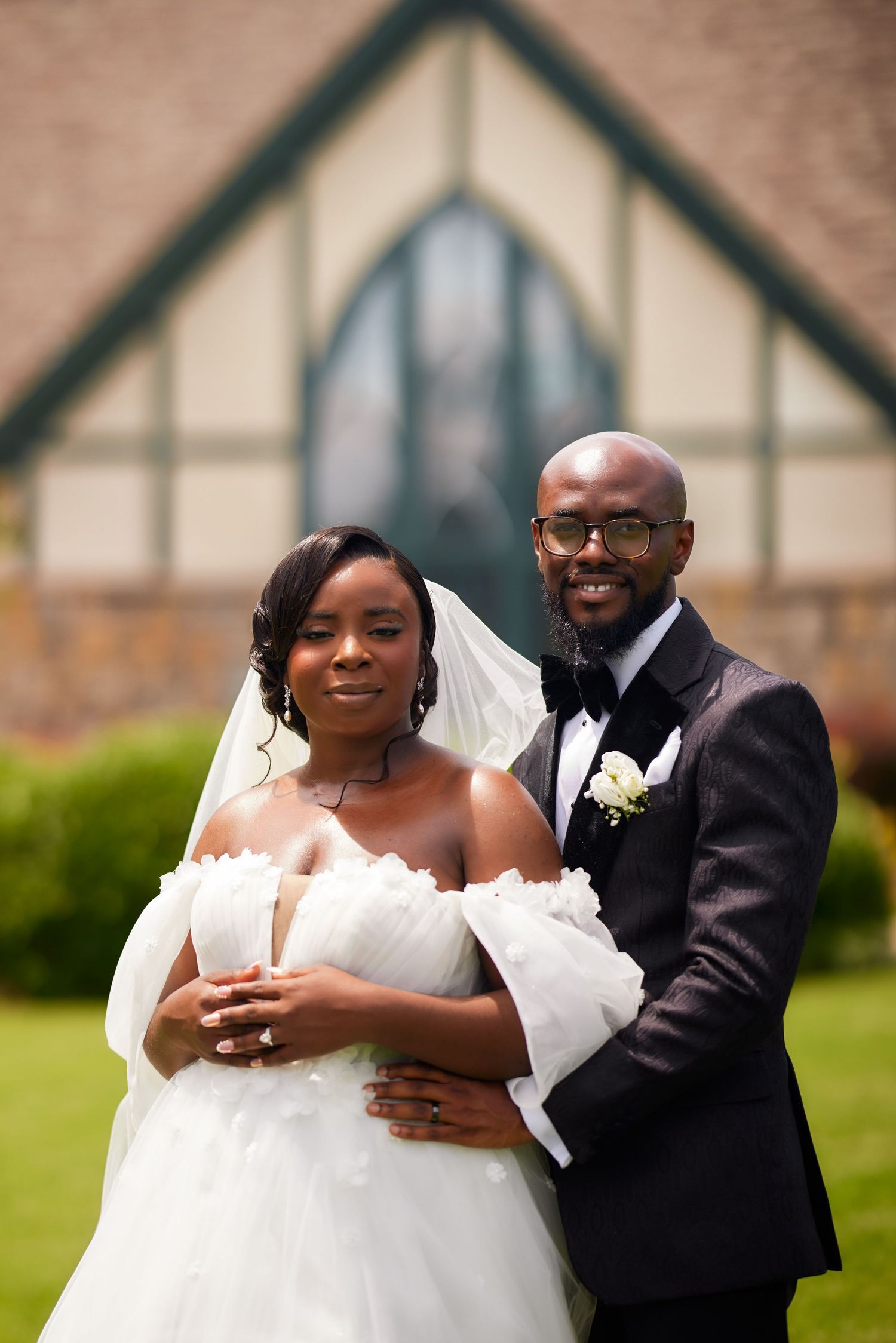 Bride and groom posing together outside a church on their wedding day, wearing formal attire.