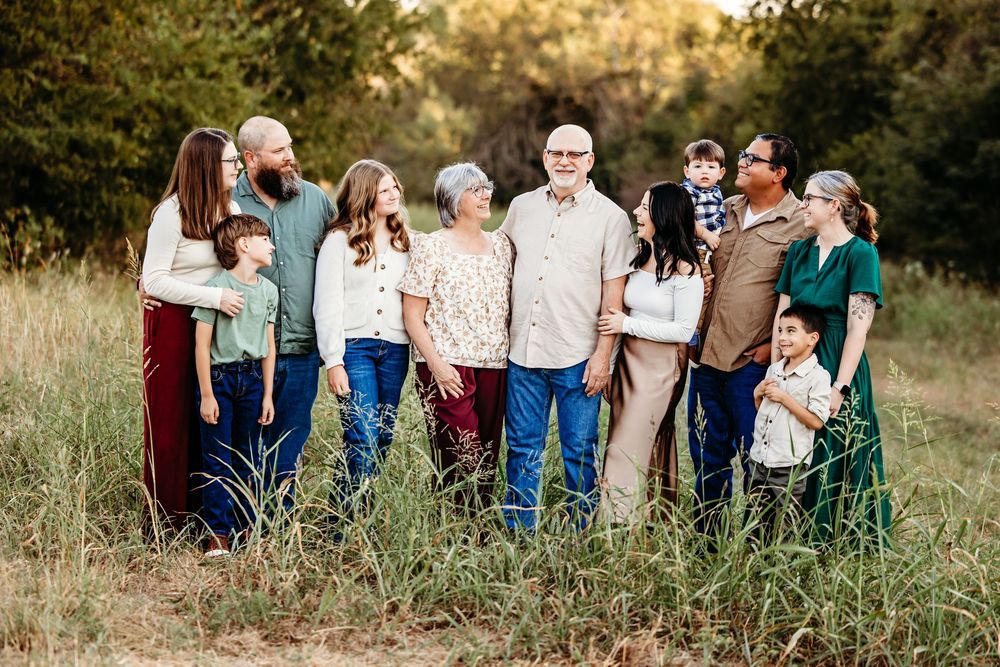 Large family group portrait outdoors in a field, spanning multiple generations, smiling together in casual attire.