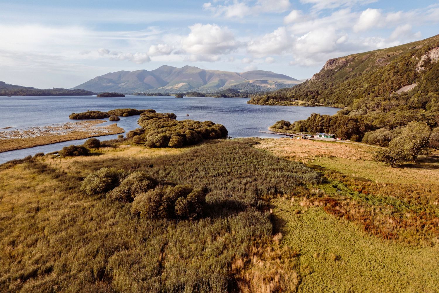 Aerial view of a scenic Irish loch surrounded by lush greenery and mountains under a partly cloudy sky.