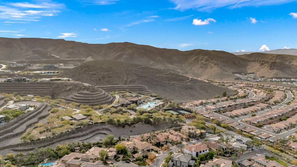 Aerial view of a residential desert community with mountain backdrop, winding roads, and lush green oasis.