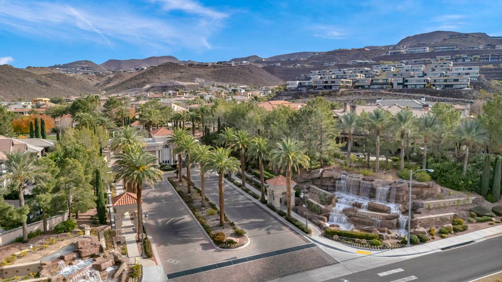 Elegant community entrance with tall palm trees and decorative waterfall feature against mountain backdrop.