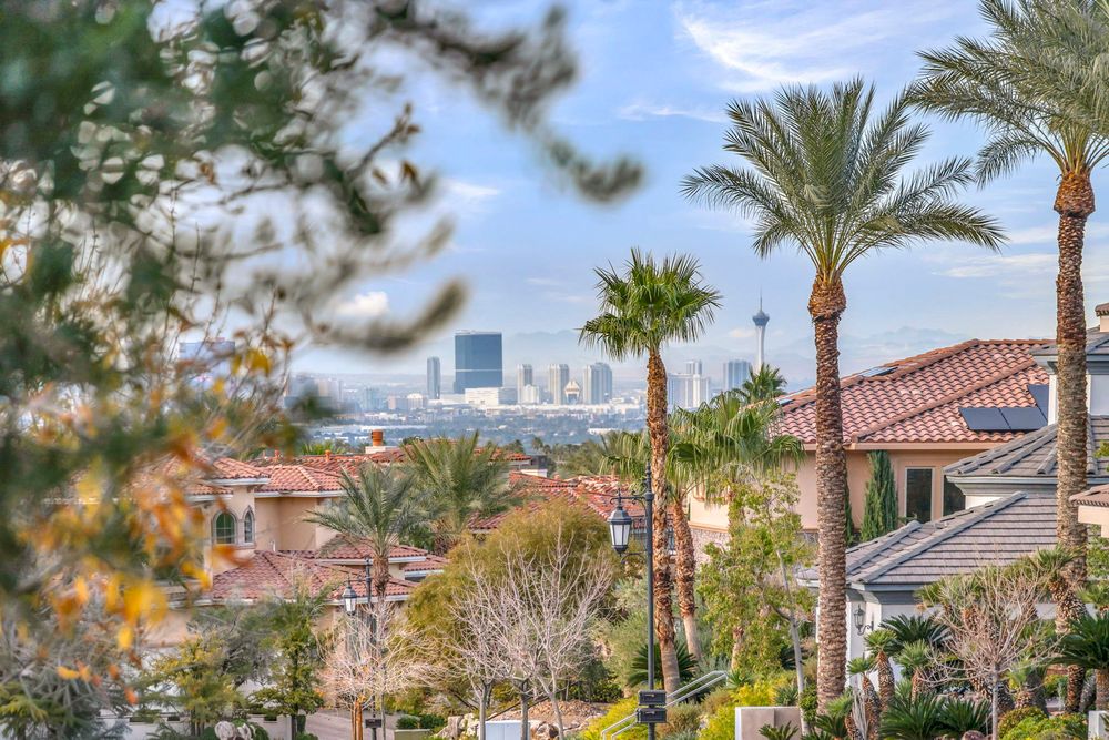 Las Vegas Strip skyline panorama framed by palm trees and red-tile rooftops of luxury homes.