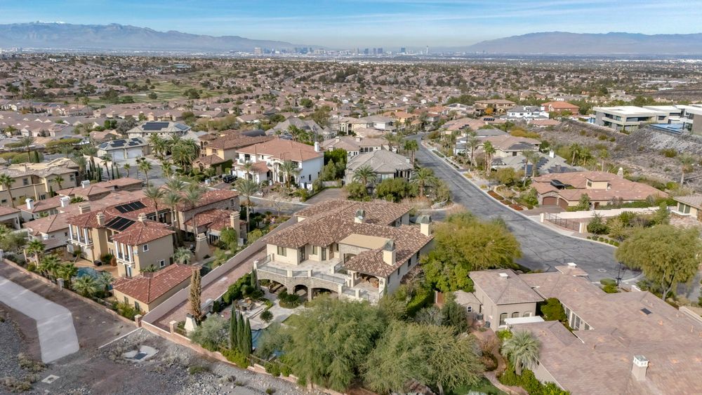 Aerial view of luxury Mediterranean-style homes in a Las Vegas suburban neighborhood with mountain backdrop.
