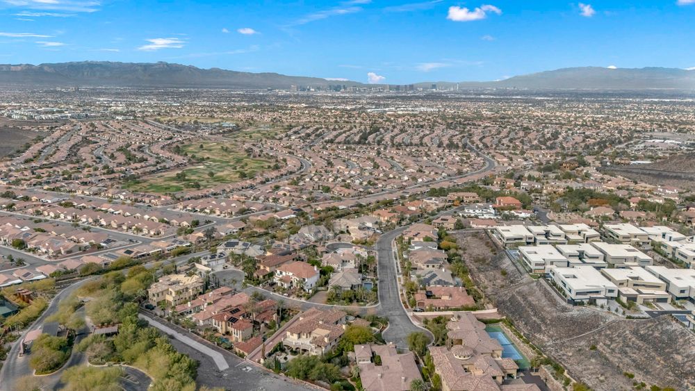 Bird's-eye view of sprawling Las Vegas suburban neighborhood with tile-roof homes and mountain views.