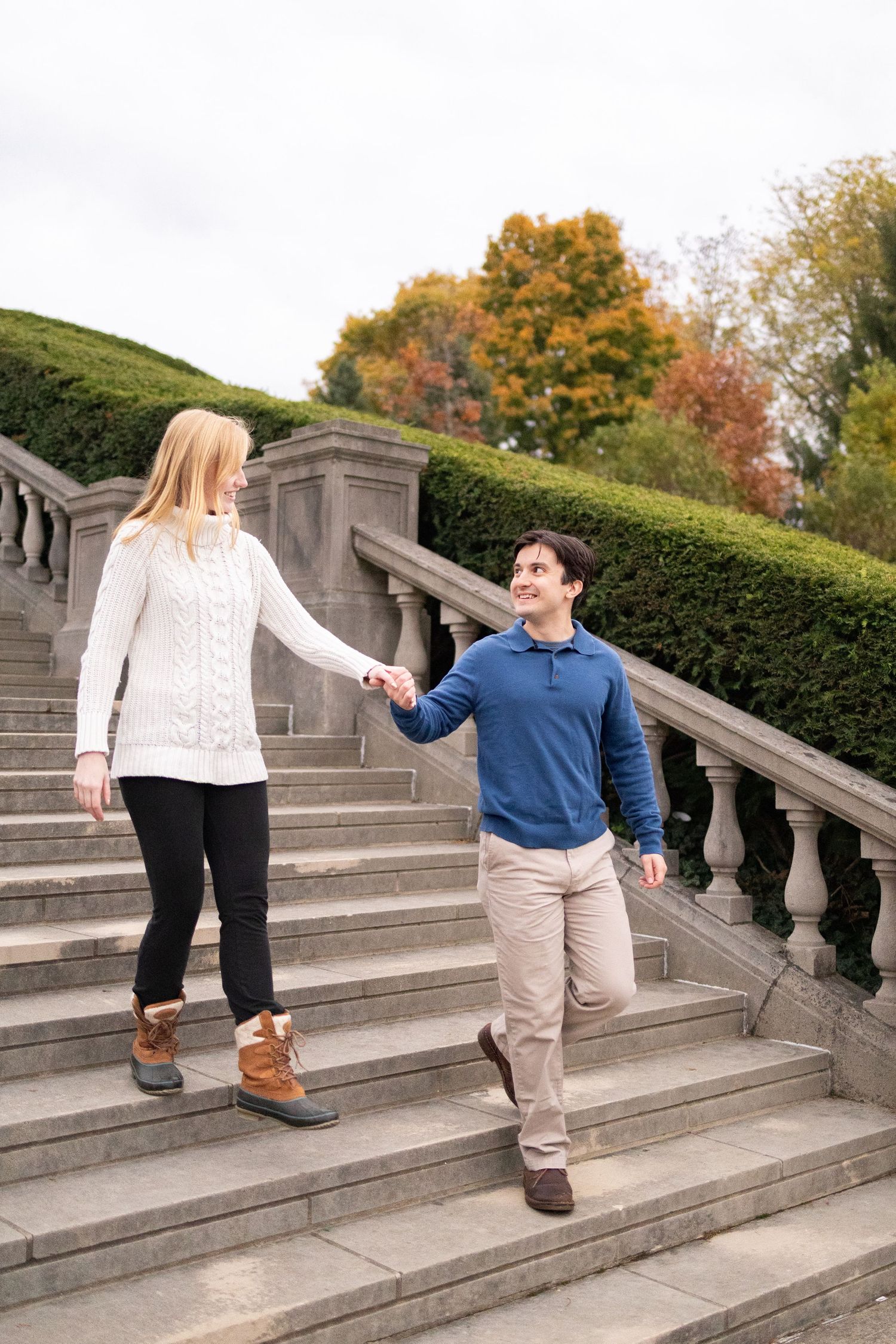 Couple holding hands walking down stone steps in Ault park, woman in white sweater, man in blue pullover.