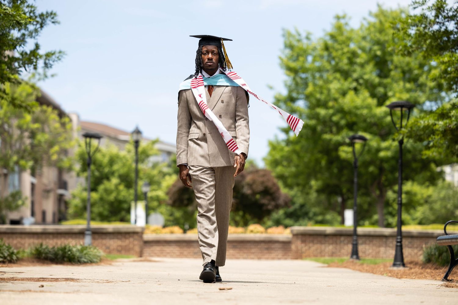 Smiling graduate wearing Indiana University stole and kente cloth scarf in tan suit outdoors.