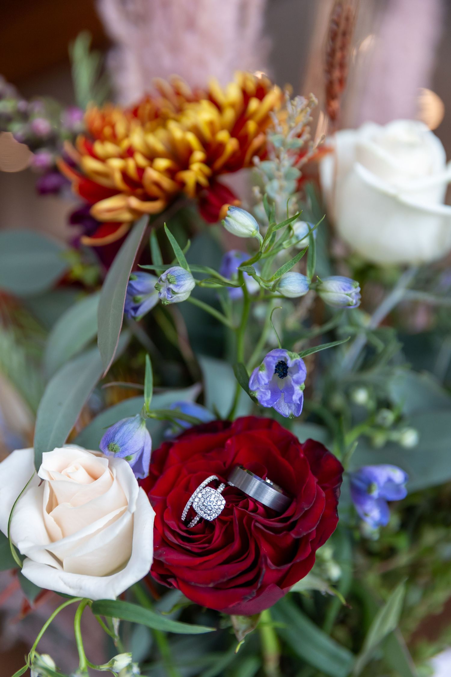 Elegant wedding flat lay featuring a bridal bouquet of blush roses, white heels, and a diamond ring in a wooden hexagonal box.