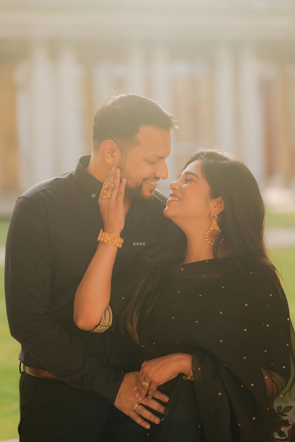 Couple in black outfits sharing a romantic moment outdoors, woman touching man's face, golden sunlight backdrop.