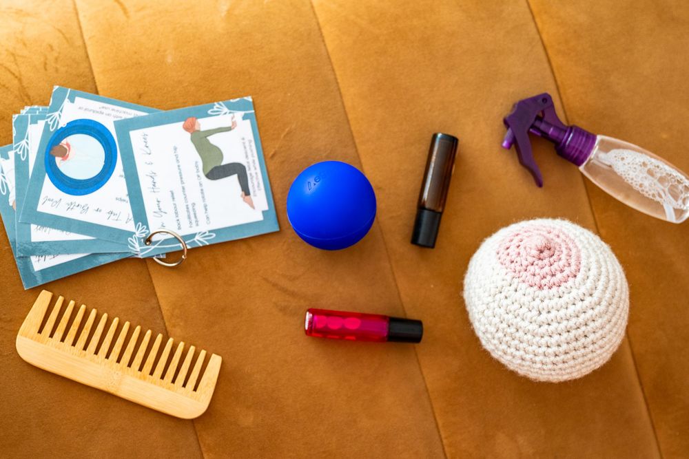 Flat lay of yoga cards, blue ball, essential oils, spray bottle, wooden comb, and crocheted kippah on brown leather.