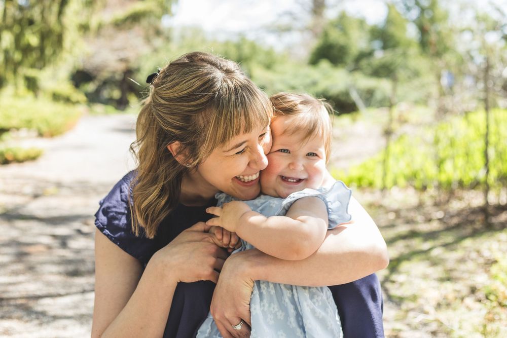 A joyful mother hugging and smiling with her happy baby girl outdoors in a sunny green park.