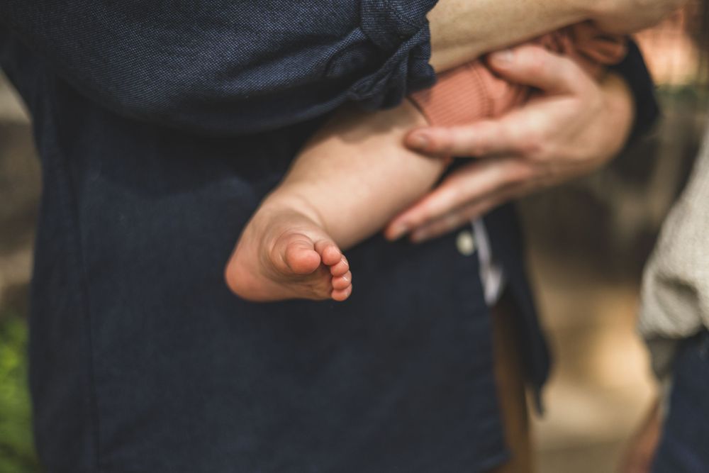 Close-up of a newborn baby's tiny feet being cradled gently in an adult's hands outdoors.