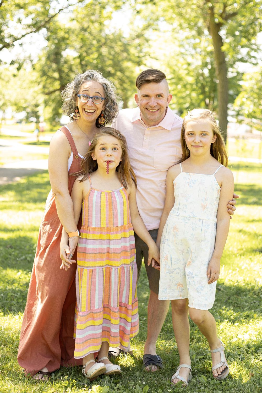 Happy family of four posing together outdoors in a green park on a bright sunny day.