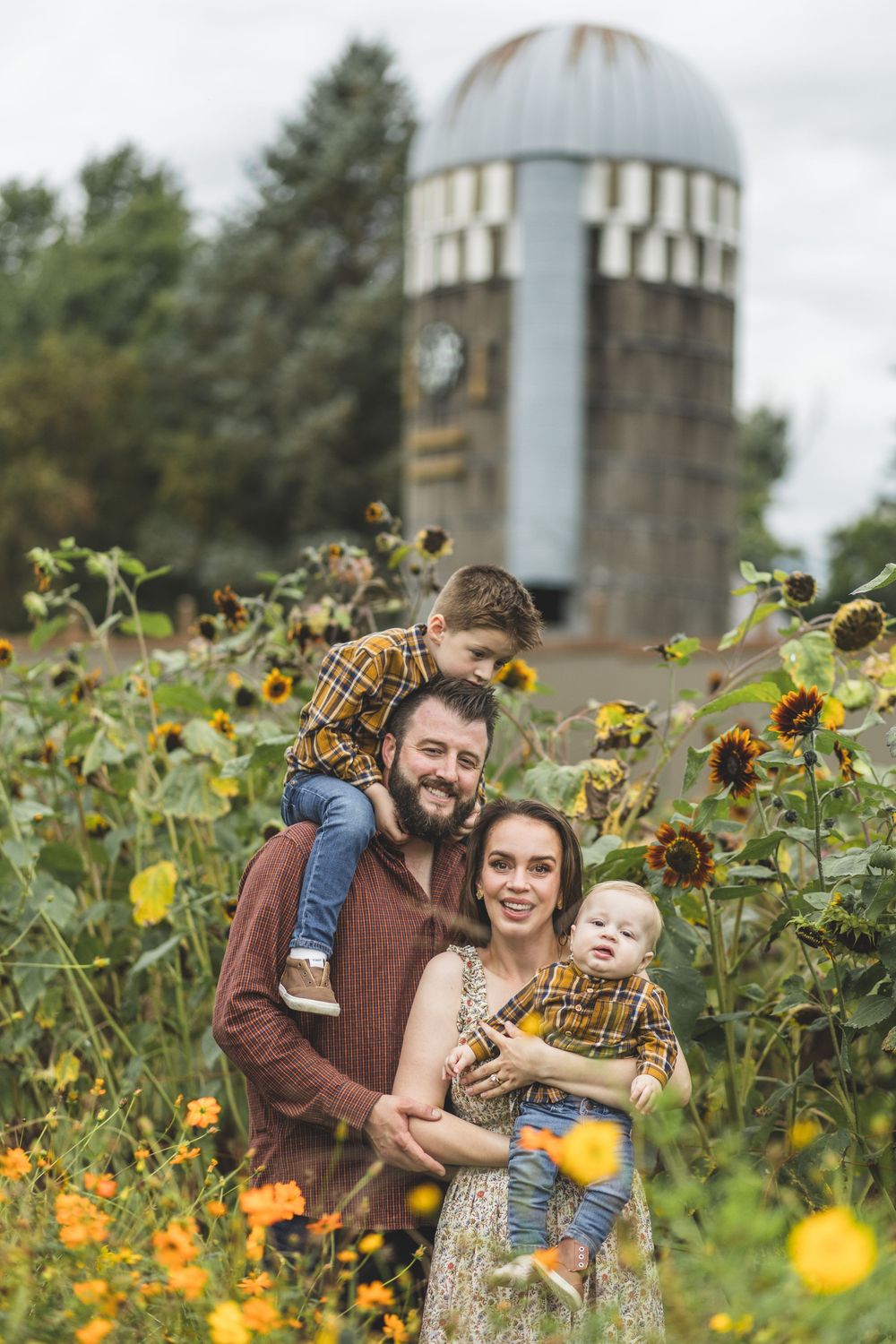 Happy family of four surrounded by sunflowers with a rustic silo in the background on a farm.