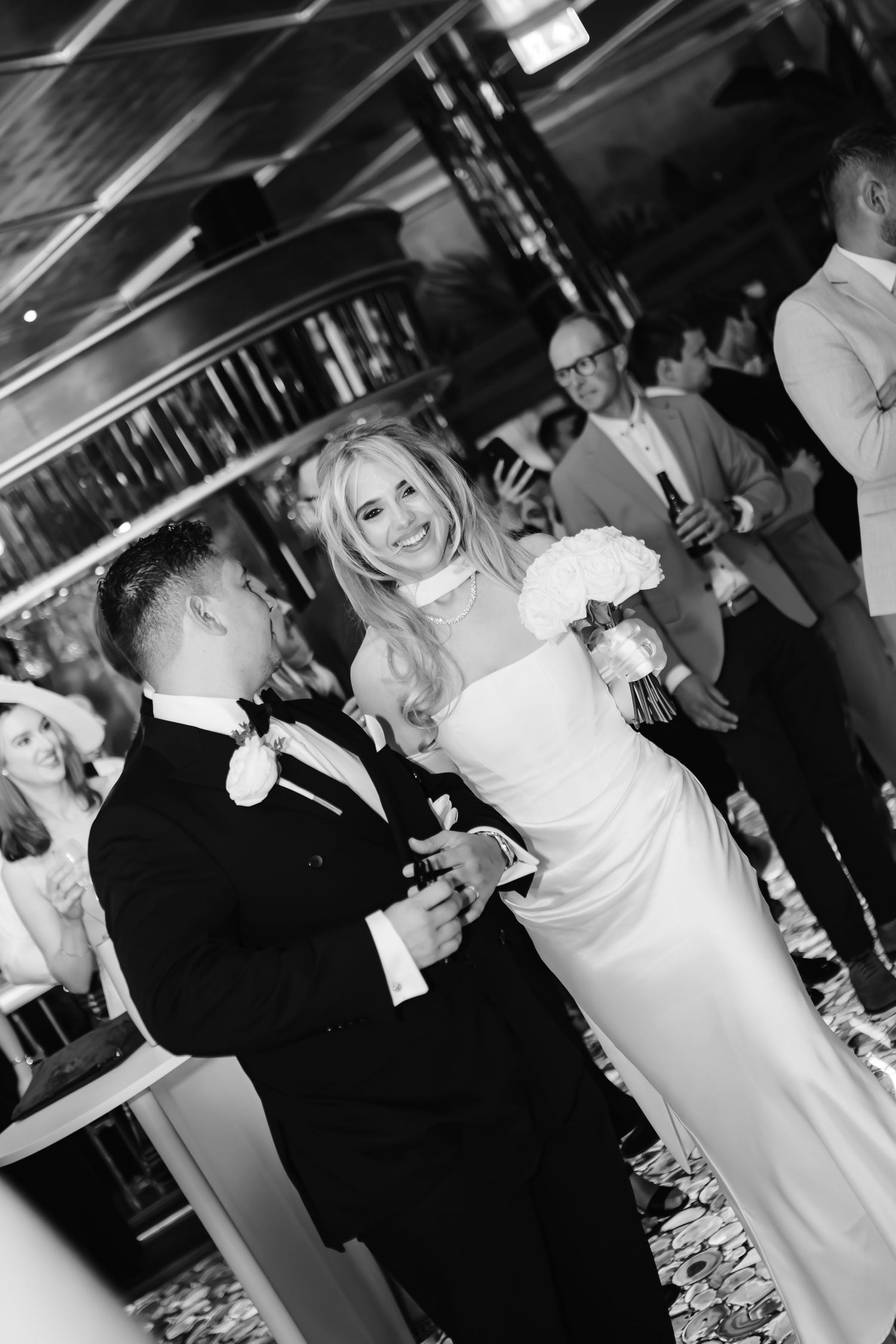Black and white photo of a smiling bride in white gown and groom in tuxedo sharing a joyful moment at their wedding reception.