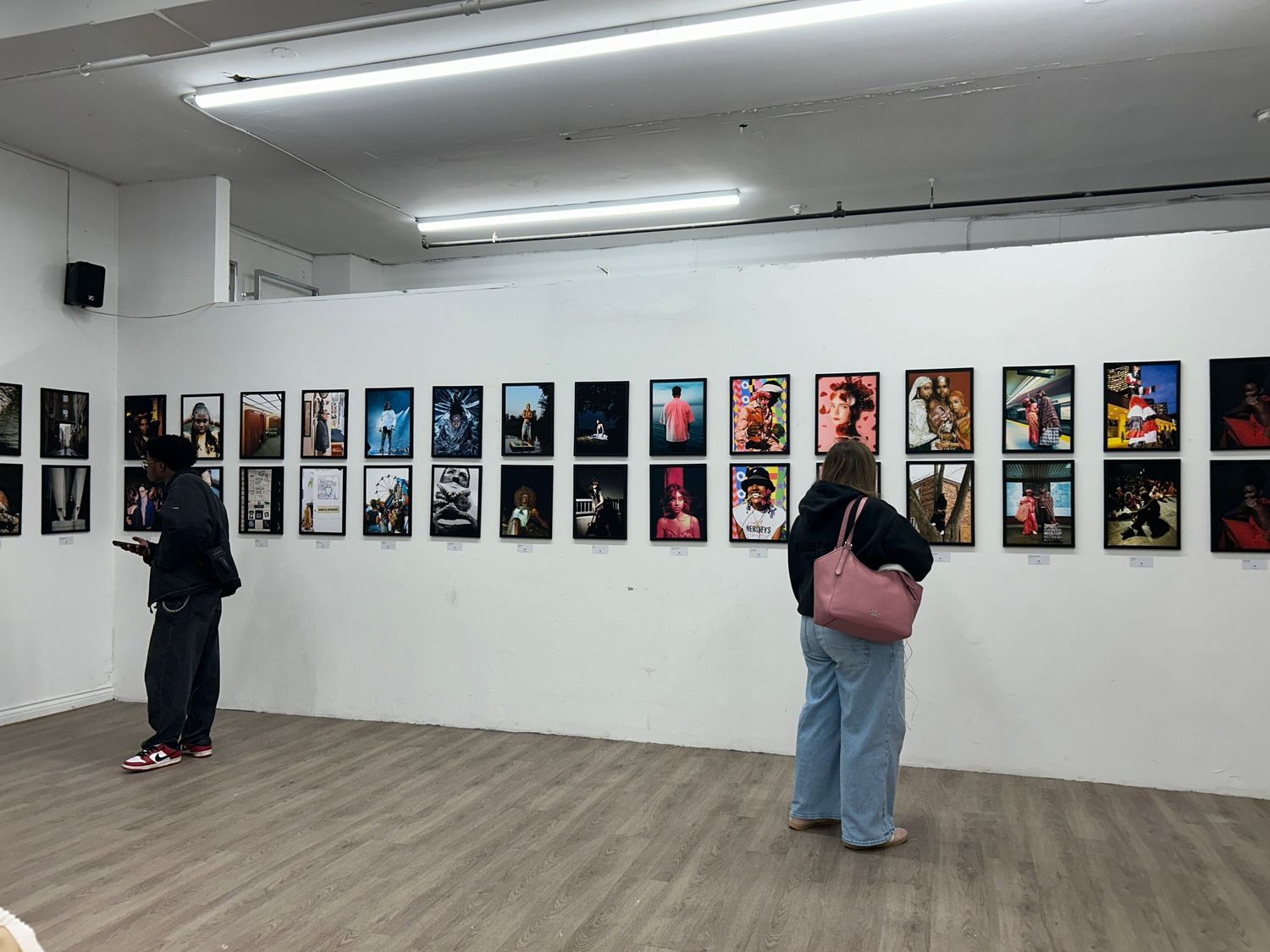 A gallery wall with many printed photographs with black frames with two people looking at it