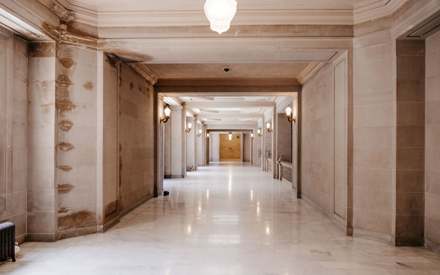 Grand marble hallway with ornate columns, wall sconces, and polished floors in a classic government building interior.