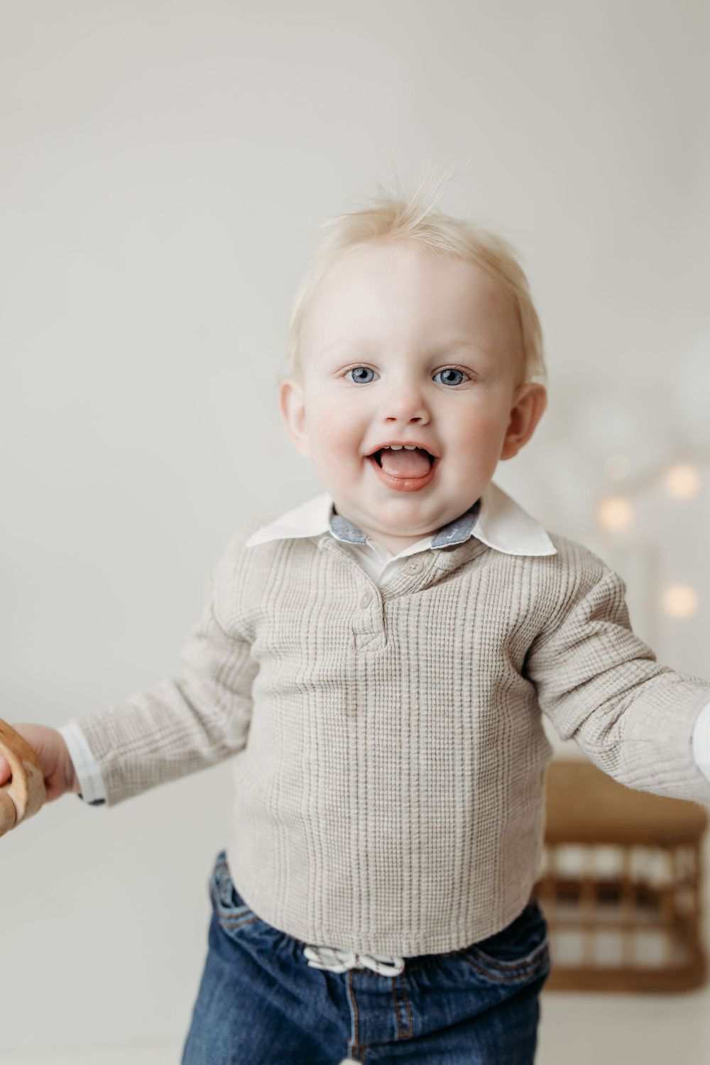 Smiling blonde toddler boy in a plaid shirt and jeans reaching out his hand.