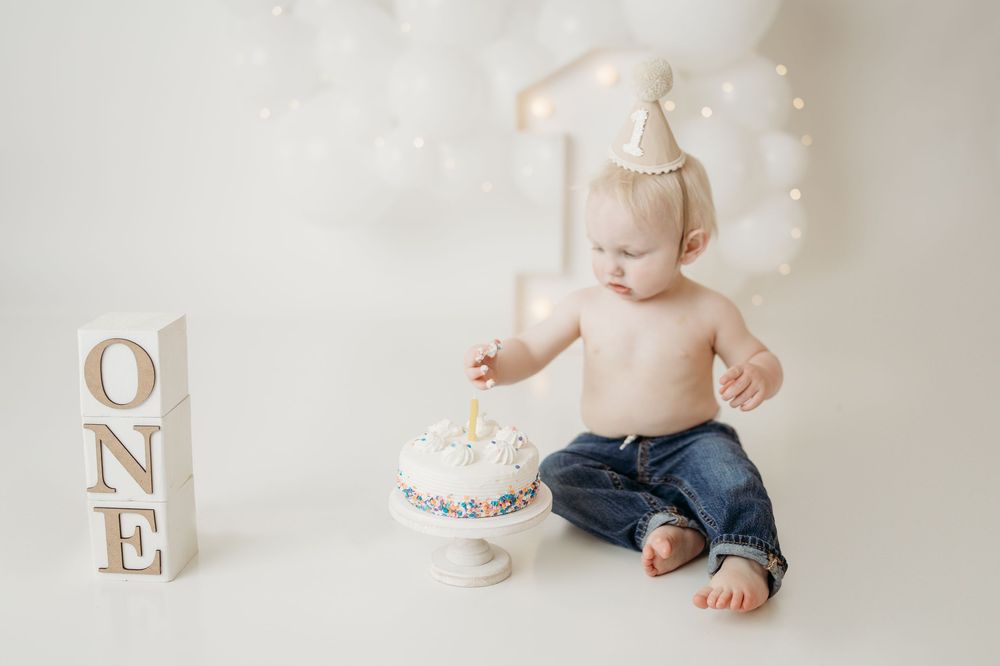 Baby's first birthday cake smash photo with white cake, balloon backdrop, and wooden ONE blocks.