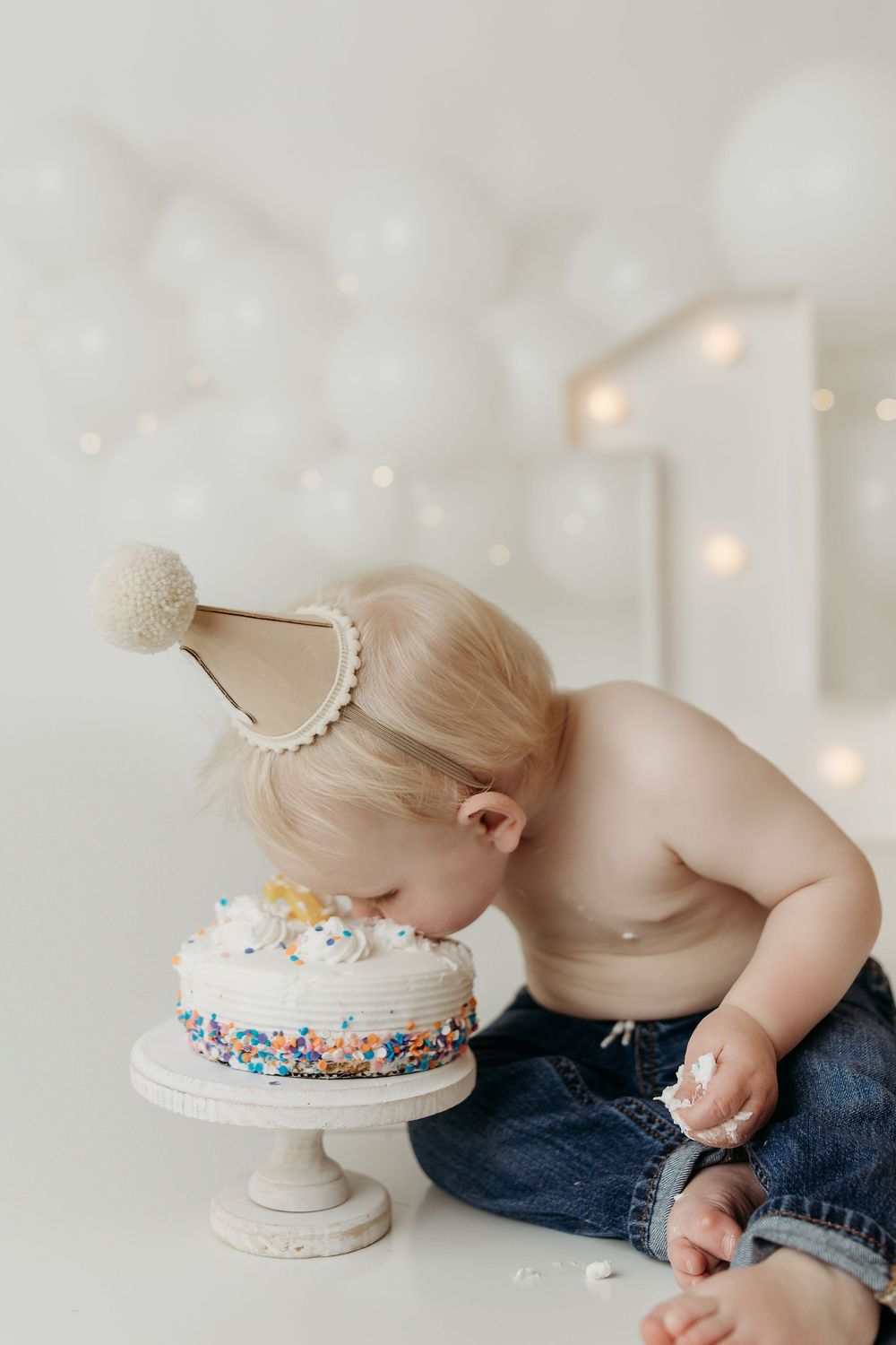 Baby boy in a party hat smashing his face into a first birthday cake.