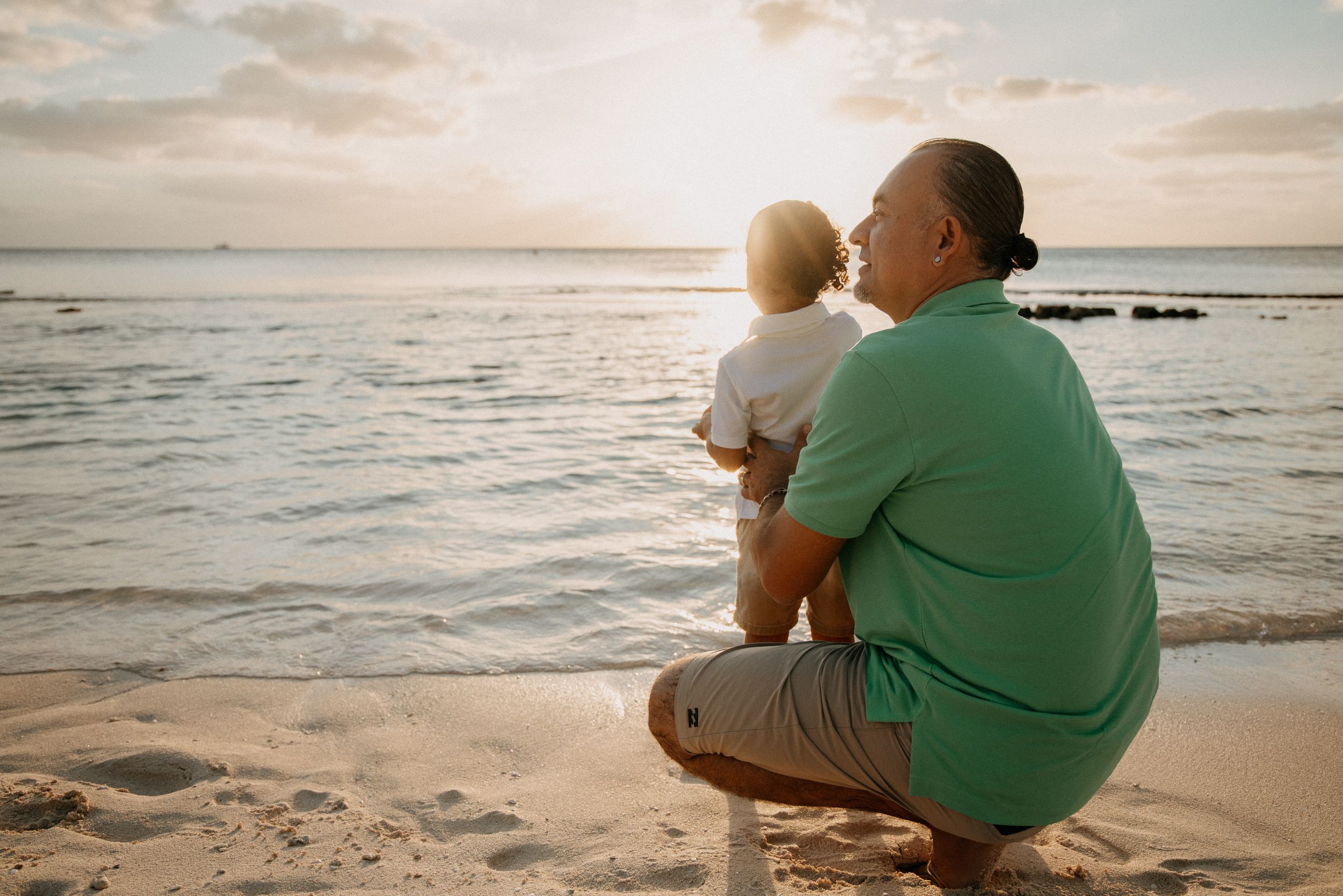 A peaceful beach scene at sunset with two figures sitting on the sand watching the ocean waves.