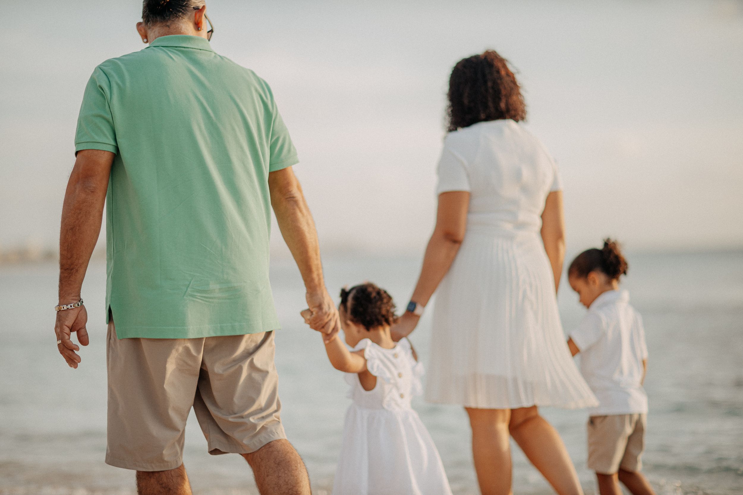 A family walking hand in hand along the beach at sunset wearing coordinated white and green outfits.