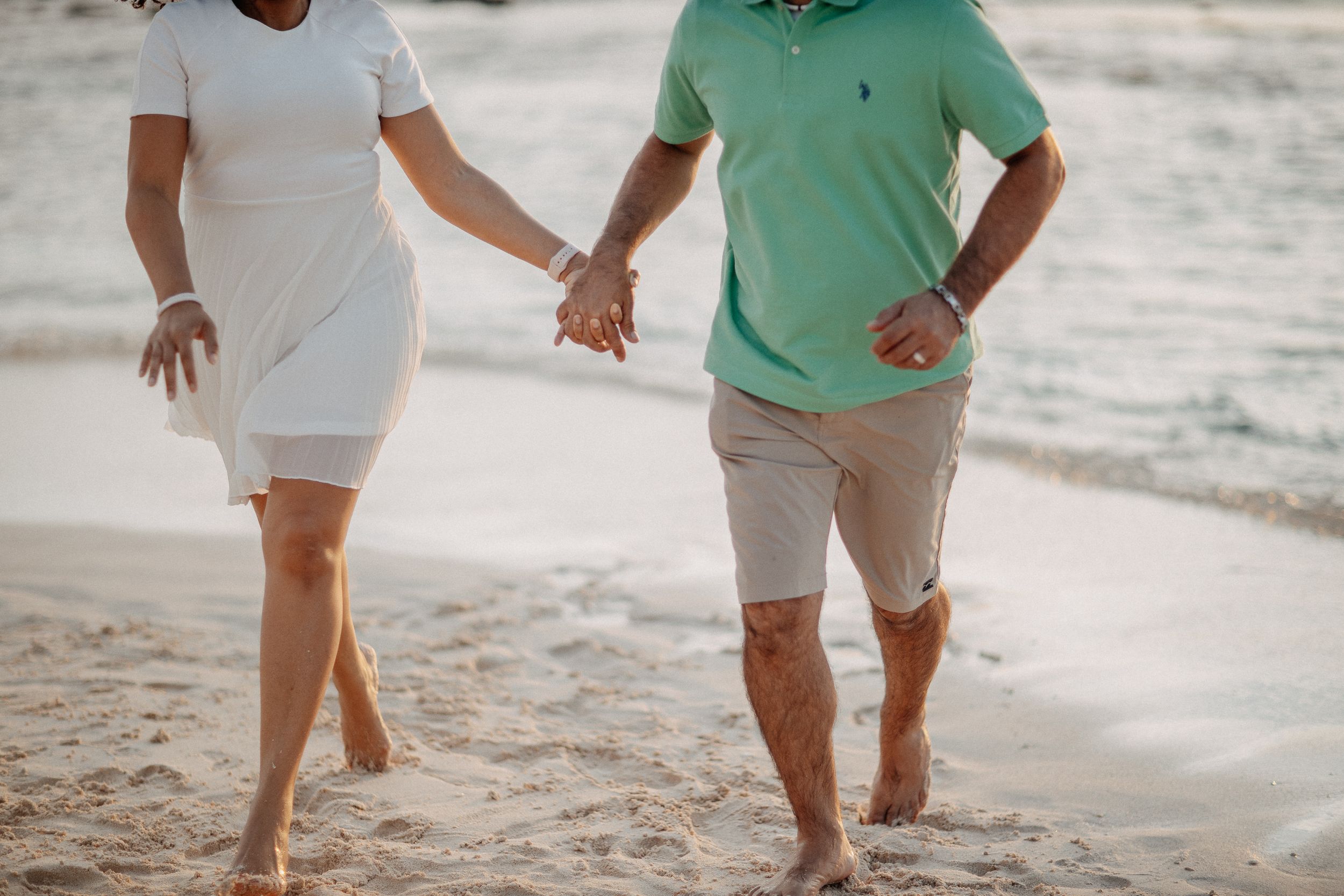 Two people holding hands while walking barefoot on a sandy beach.