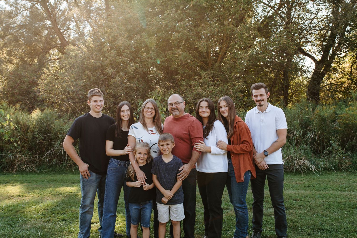 Multi-generational family gathering outdoors for a group portrait at sunset in a garden setting.