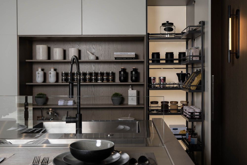 Modern kitchen interior with sleek black cabinets, stainless steel appliances, and open shelving displaying organized cookware.