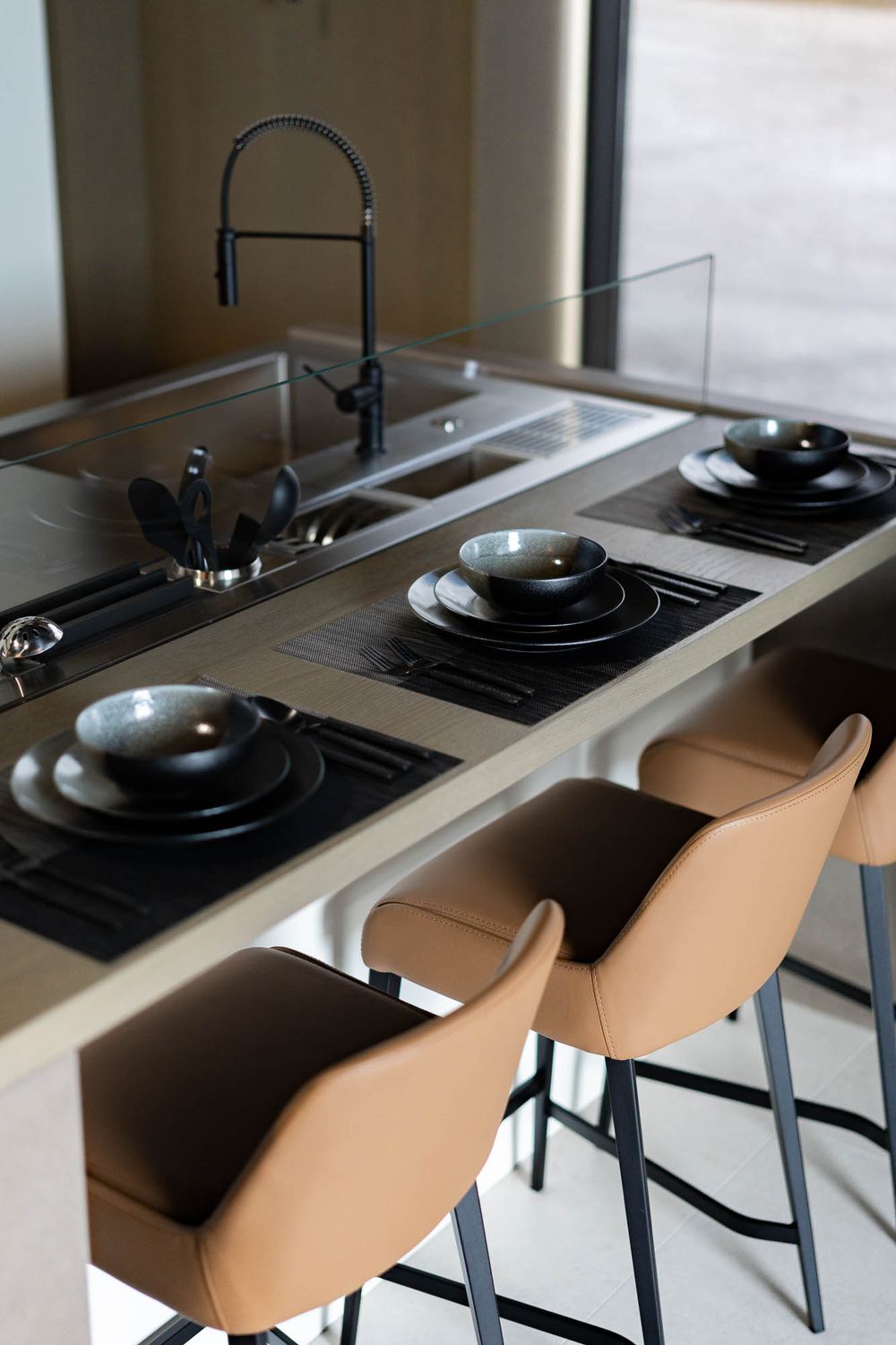 Modern kitchen counter with sleek black stovetop and beige bar stools arranged in a minimalist design.