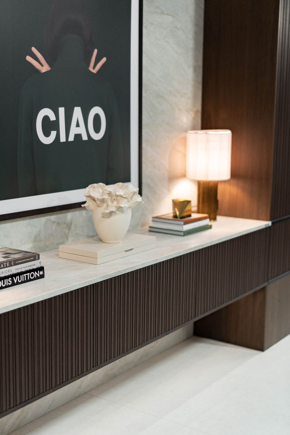 Minimalist shelf display with Louis Vuitton book and CIAO artwork against dark wood paneling.