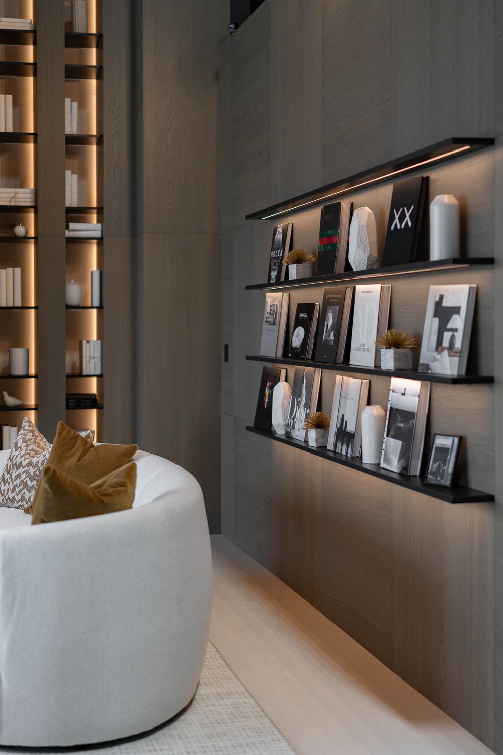 Modern living room corner with floating black shelves displaying framed photos and a cozy white curved chair with gold pillow.