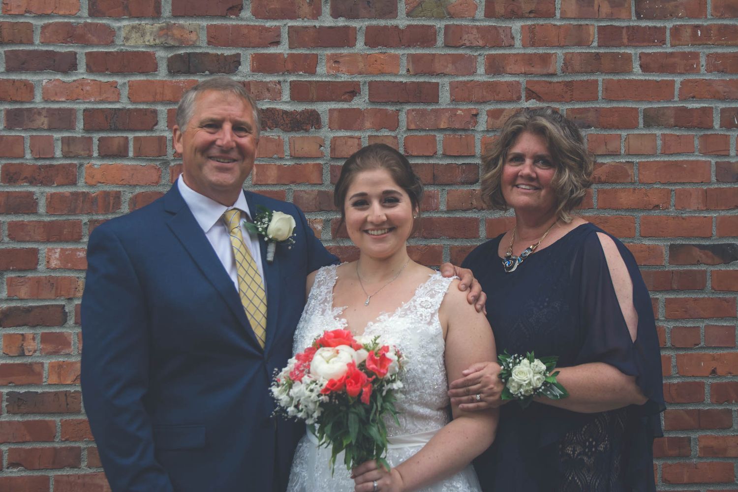 Wedding party poses against rustic brick wall during outdoor celebration.