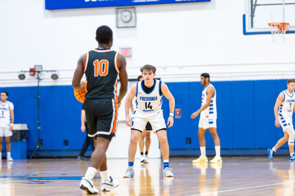 Basketball players spread across indoor court during competitive game play.