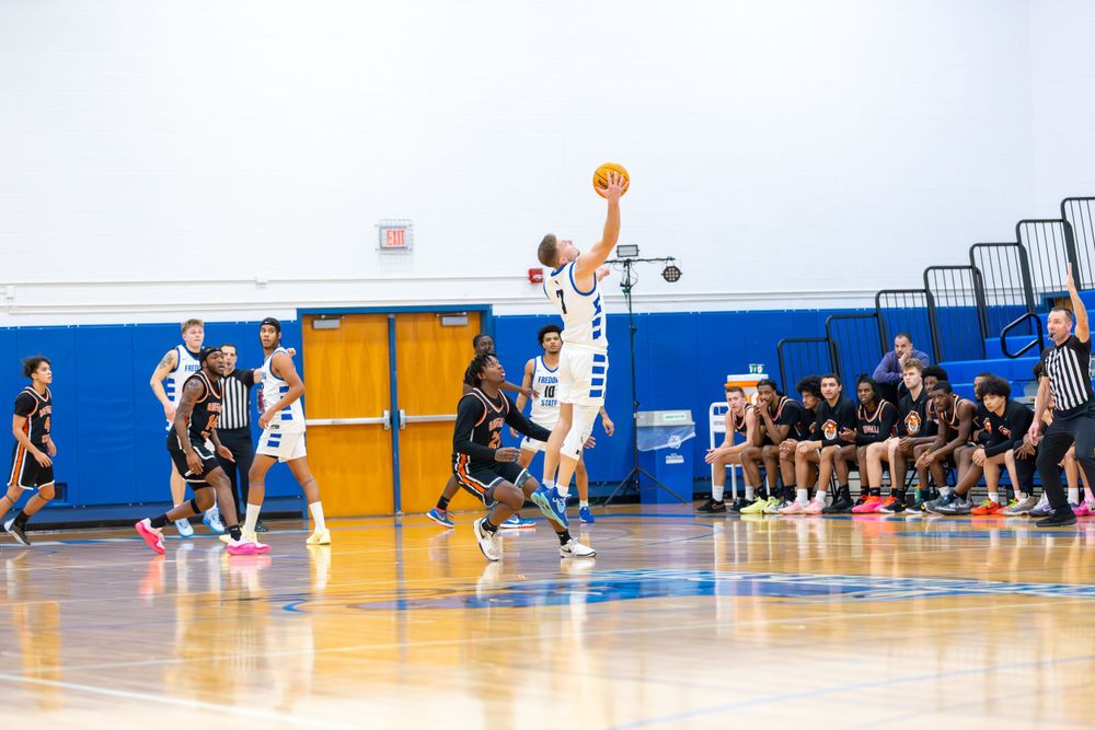 Basketball players compete on indoor court with scoreboard visible in background.