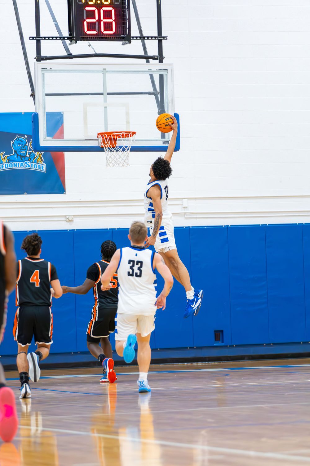 Basketball players in action on indoor court with digital scoreboard displaying time.