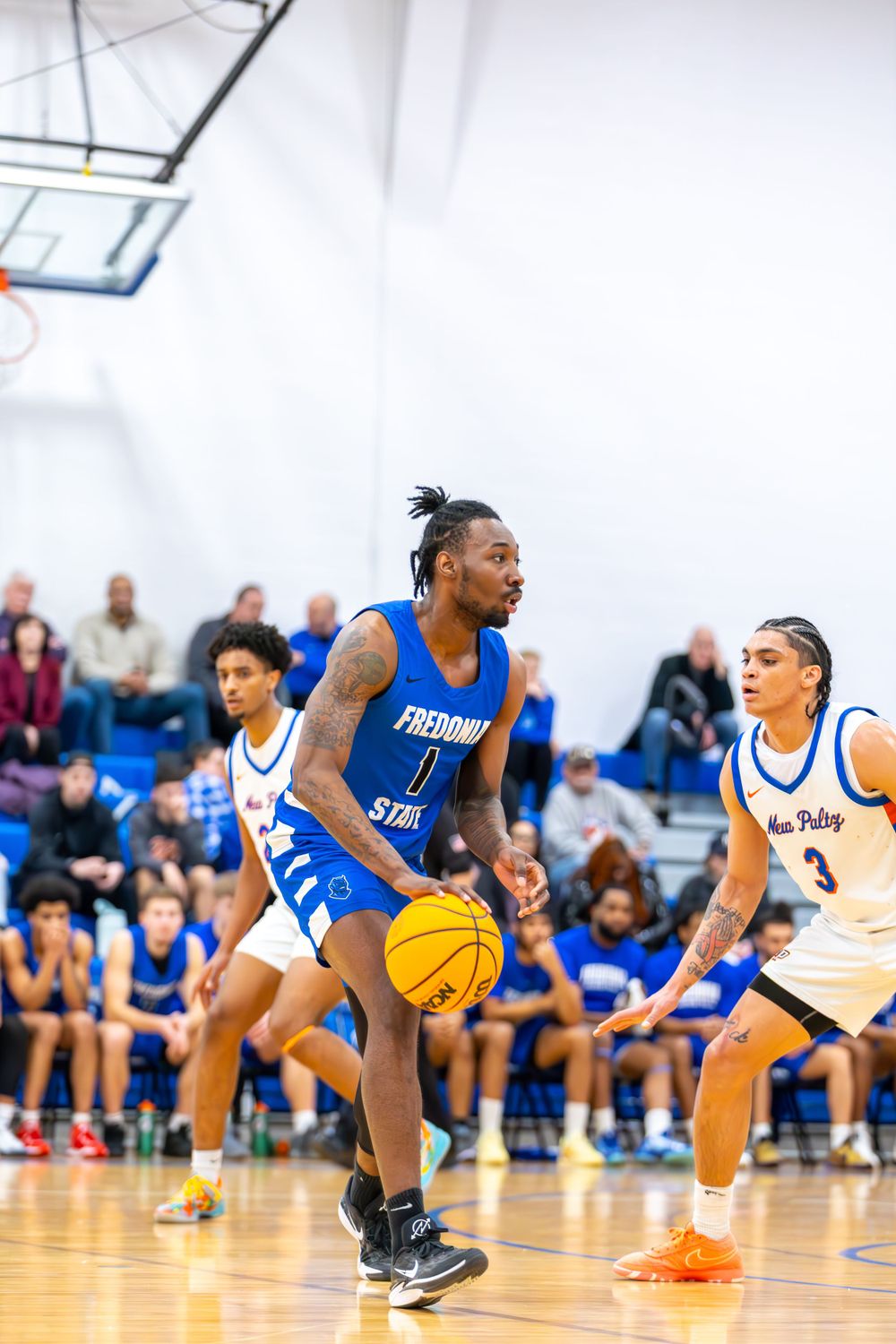 Basketball players dive for a loose ball during competitive indoor game action.