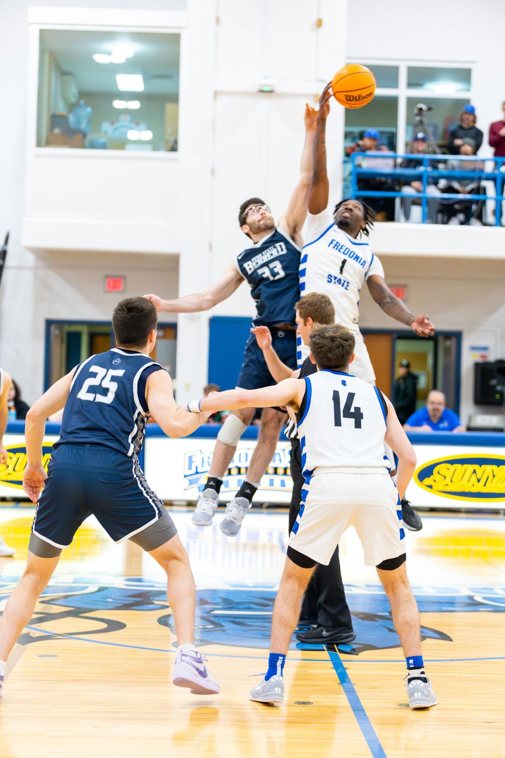 Players in navy and white uniforms compete for the ball during an indoor basketball game.