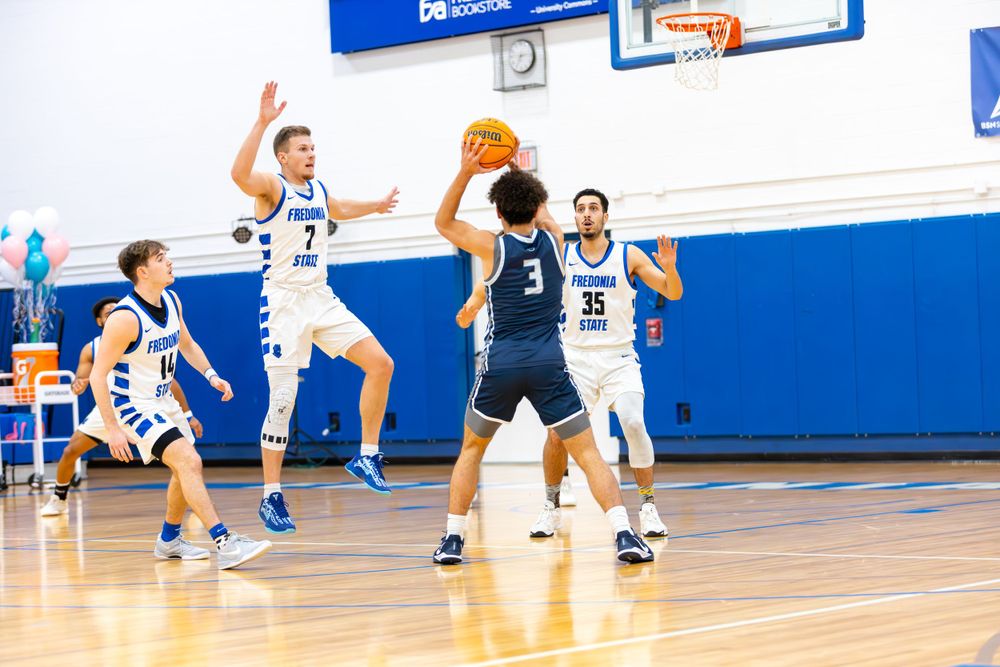 Basketball players from opposing teams position themselves during gameplay on a well-lit indoor court.