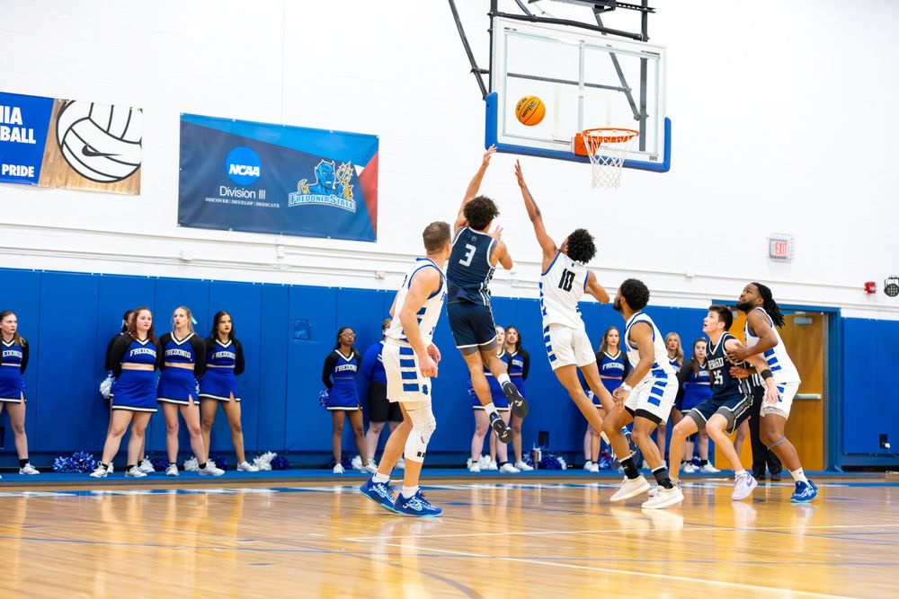 Basketball players spread across the court during an indoor game with blue walls and white accents.