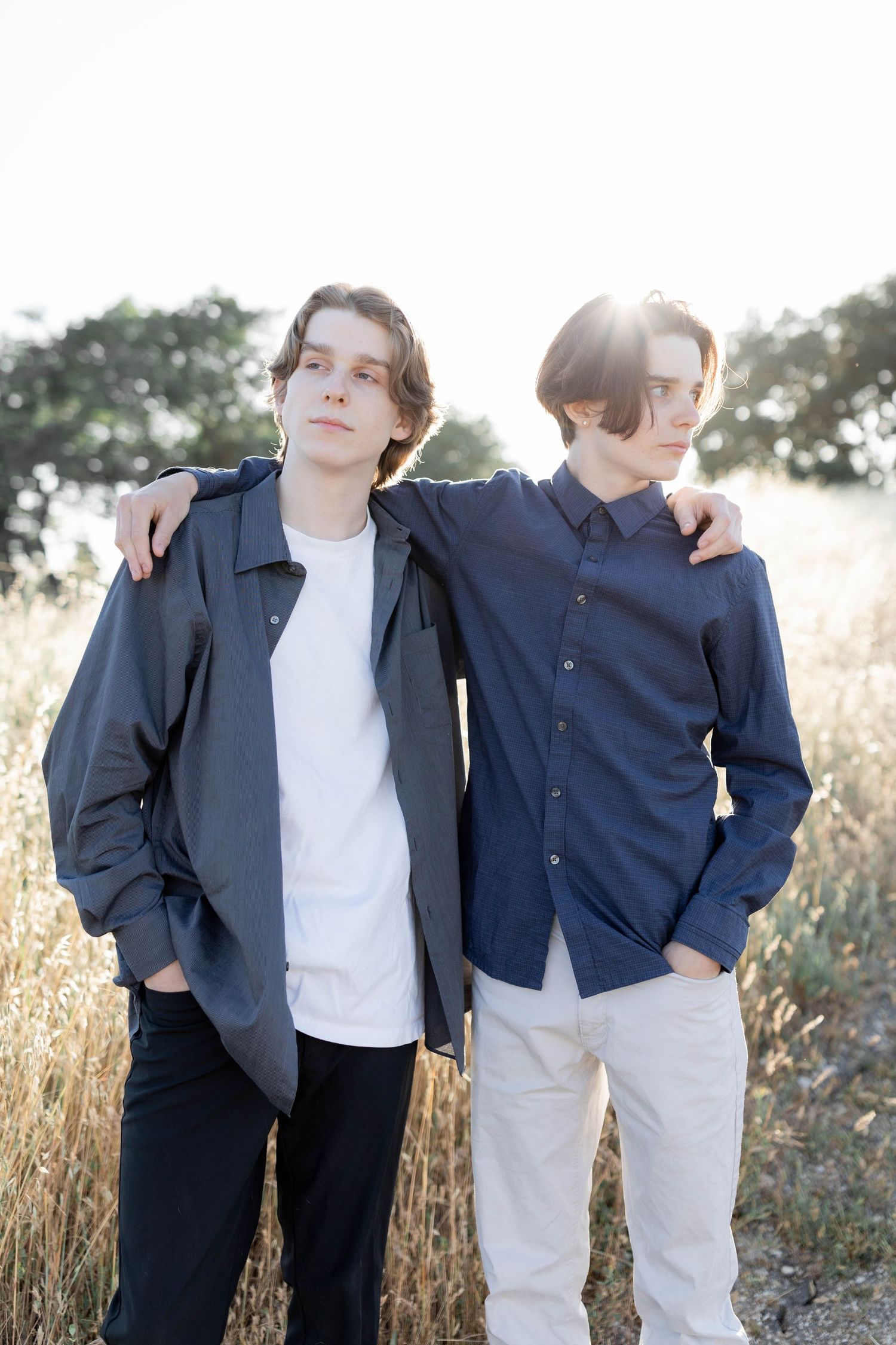 Two young men in casual attire standing together in a sunlit field.