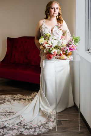Modern bridal portrait featuring white gown and colorful bouquet near burgundy velvet couch.