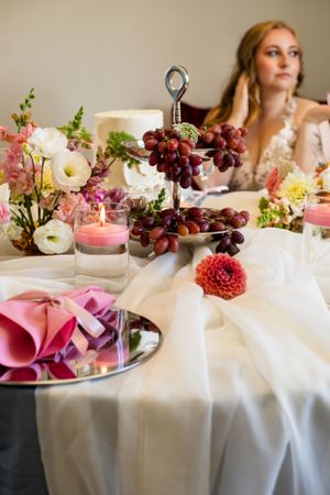 An elegant table setting with grapes, candles, and pink floral decorations on white linens.