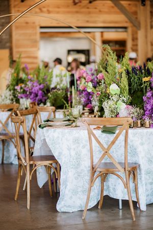 Rustic wedding reception tables set with cross-back chairs and floral centerpieces.