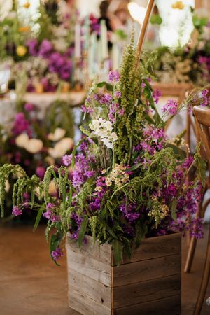 Rustic wooden box filled with vibrant purple and white wildflowers in a wedding reception setting.