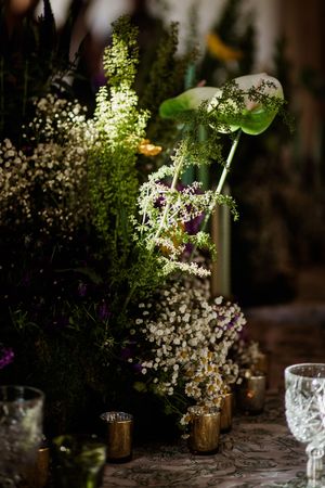 Elegant floral centerpiece with baby's breath and delicate white flowers in golden vases on a textured tablecloth.