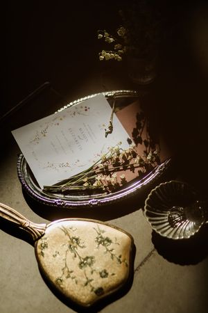 Wedding invitation with dried flowers and vintage mirror on dark moody surface.