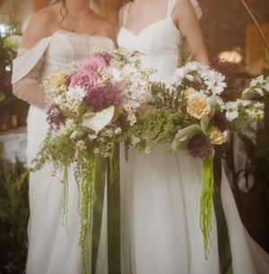 Row of white wedding dresses adorned with cascading floral bouquets and greenery.