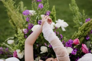 Raised arms against purple and white floral backdrop at outdoor celebration.