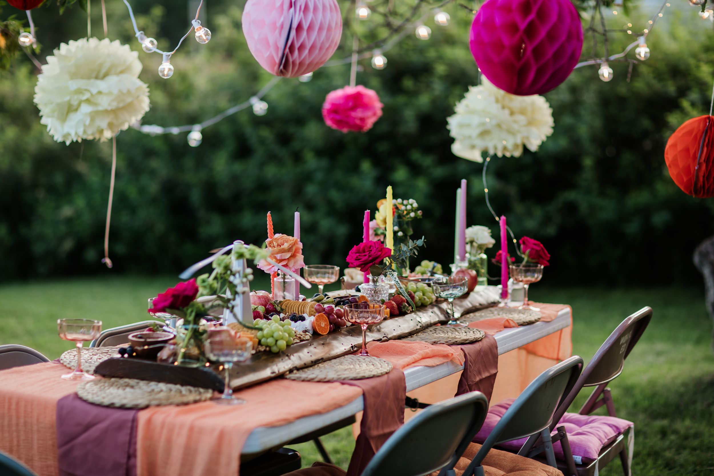 Outdoor table setting with pink and white paper lanterns and string lights creating a festive atmosphere.