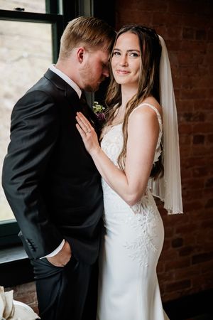 An intimate wedding moment captured against a brick wall and window backdrop.